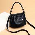 Black cloud crossbody bag with pleated texture and silver heart charm on beige background - Black