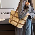 Minimalistische Stroh-Tote-Bag mit braunen Lederriemen und Goldnieten an einem Modell - Khaki