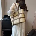 Stroh-Stofftasche mit braunem Ledergitter und Metallnieten, getragen von einem Modell - Cremeweiß