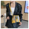 Detail of striped bucket bag with yellow faux leather trim worn by a model in black suit - Green