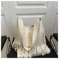 Detail van beige hobo-tas met lange franjes en litchi-textuur op een leren stoel - Wit