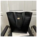 Dettaglio della grande borsa tote nera effetto coccodrillo con logo in oro su sedia - Nero