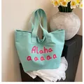 Mint green canvas tote bag with pink artistic lettering shown in a floral lifestyle setting - Green