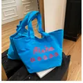 Détail du sac cabas en toile bleu vif avec lettrage rose sur un sol en bois clair - Bleu