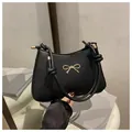 Minimalist black faux leather hobo bag with gold bow detail and knotted shoulder strap - Black