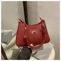 Dark red minimalist shoulder bag with a gold bow accent and a thick knotted strap - Red