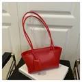 Detail of red leather tote bag with long straps and charm on white book prop - Red