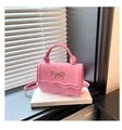 Macro view of pink faux leather bag featuring golden bow detail and wavy edge design - Pink