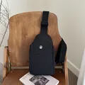 Chic black nylon crossbody chest bag for women with silver logo and wide strap on wood chair - Black
