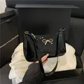 Elegante bolso de hombro en charol negro con un detalle de lazo dorado metálico - Negro