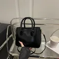 Glossy black leather tote bag with round handles and adjustable strap on a modern shelf - Black