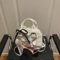 Creamy white underarm bag with black bow and lace trim in a modern interior setting - White