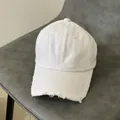 Detailed close-up of distressed ripped edges on a white washed denim baseball cap - Adjustable / White