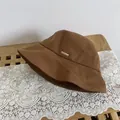 Detalle de gorro de pescador en lona marrón oscuro con una placa de metal dorada - M / Caqui