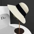 Detail of a beige woven straw sun hat with a black ribbon on a gold metal stand - M(56-58cm) / White