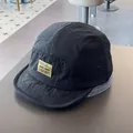 Close-up of black 5-panel camper hat featuring a yellow woven patch and metal eyelets - M / Black