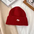 Primer plano de un gorro de punto rojo con bordado de alce blanco sobre un fondo acogedor - M(56-58cm) / Burdeos