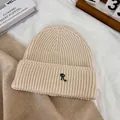 Détail du bonnet en tricot côtelé beige avec broderie R noire sur un fond de style de vie - M / Beige