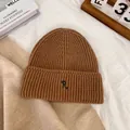 Detailed close-up of brown ribbed knit beanie with R-letter embroidery on white fabric - M / Khaki