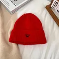 Detalle de gorro de punto rojo con bordado de gato azul sobre ropa de cama blanca - M / Rojo