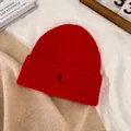 Détail d'un bonnet en tricot rouge avec broderie R noire sur un fond texturé chaleureux - M / Rouge