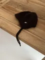 Close-up of fluffy dark brown knit wool hat with metallic logo tag on rustic wood - M / Coffee