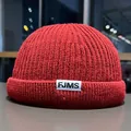 Detailed macro of a deep red ribbed knit beanie with a woven white FJMS logo tag - M / Red