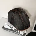 Detalle de boina denim con costuras naranjas y borde de cuero marrón sobre libros - M / Negro