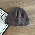 Close-up of distressed knit beanie with silver rings and safety pin on wood - Gray