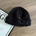 Detail of black knit beanie with distressed holes and silver rings on wood surface - Black