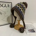 Close-up of Fair Isle knit winter hat with ear flaps and fluffy brown pompoms on wooden stand - M (56-58cm) / Coffee