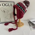 Dettaglio del cappello in maglia bordeaux con motivi geometrici, nappe e un pompon - M (56-58cm) / Borgogna