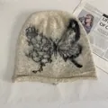 Close-up of cream knit beanie featuring black butterfly jacquard and fuzzy mohair texture - M (56-58cm) / Off White