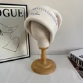 Detalle del gorro de punto crema con costuras en contraste morado y bordado de arcoíris - M / Blanco