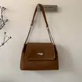 Detail of brown leather handbag with silver metal buckle hanging on a wall hook - Brown
