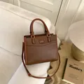 Vintage braune Lederhandtasche mit runden Griffen und verstellbarem Gurt auf einem Sofa - Dunkelbraun