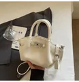 Detailed close-up of cream-white leather bucket bag with rotating metal clasp and top handle - White