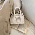 Vue détaillée d'un sac seau en toile beige sur un livre avec un style vintage élégant - Sans pendentif / Blanc