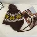 Detail of knit snowflake pattern and ear flaps with tassels on a brown winter beanie - M / Coffee