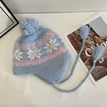 Detailed close-up of light blue knit hat featuring pink snowflake patterns and soft pom-poms - M / Light Blue