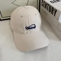 Close-up of beige cotton baseball cap featuring navy blue Rainbow cursive embroidery detail - White