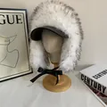 Detail of faux fur trapper hat with black peak, bow strap and plush winter texture - White
