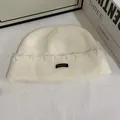 Textura detallada del gorro de punto acanalado blanco roto con etiqueta negra minimalista - M (56-58cm) / Blanco