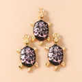 Macro detail of three sea turtle pendants with pink floral enamel and gold plating - Black and Pink Turtle