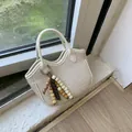 Cream woven bucket bag with beaded charm detail and dual handles in soft sunlight - White With Wood Bead Pendant