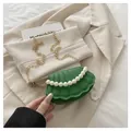 Close-up of green shell-shaped bag with pearl handle and golden chain on beige fabric - Green