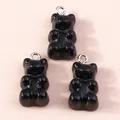 Close-up of three black gummy bear resin pendants with silver jump rings on pink background - Black