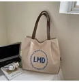 Close-up of minimalist canvas tote with blue letter embroidery and brown leather handles - One Size / Off White