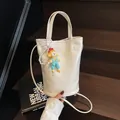 White crocodile-textured bucket bag with pearl chain and doll charm on wooden stairs - Small / White