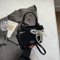 Black bucket bag with pebble leather texture, pearl charm, and chic white artistic lettering - Bow Charm Style / Black